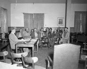 Early in 1952, every county Farm Bureau in Oklahoma was visited by state leaders in an effort to create more personal relationships between local members and the state organization. This photo was taken at one of the first conferences, which was held at the Hugo Community Center with Choctaw County Farm Bureau members. At the desk is Jack Norris, President of the Choctaw County Farm Bureau. In the background are (left to right) Lex Eddleman, John I. Taylor, Dan Arnold, Ernest Means, Clarence Adams, Glen Grubbs, Mrs. Eugene Jones, O.T. Eddleman, Mart Fowler, E.A. Kissick, and Rolly Morris.