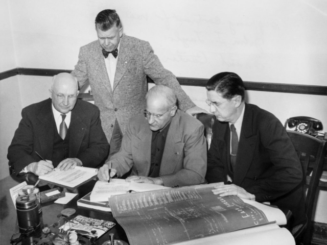 Oklahoma Farm Bureau recognized the need for a larger building to house the ever-expanding organization. On February 9, 1953, a contract was signed for construction of a new building near the Oklahoma State Capitol. Here, OKFB President John I. Taylor (seated center) signs the contract, while Charles M. Suttle, the contractor (left), signs another copy. Frank Carter (standing) and Martin Lawrence, architect, look on.