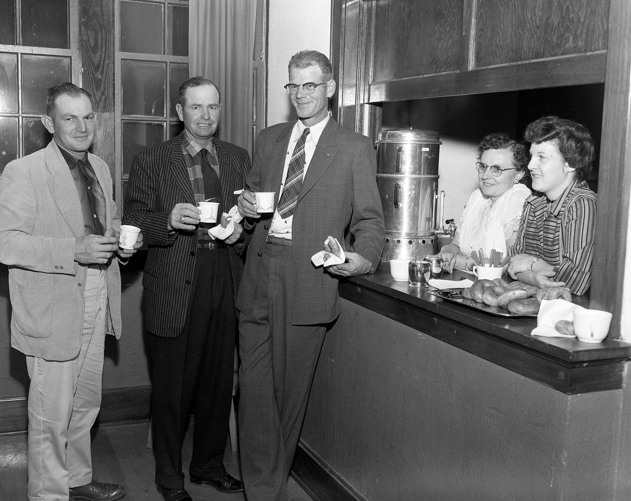 D.G. Meier Jr., Bennie Tice and Orval Swain enjoy coffee and doughnuts provided by Mrs. O.E. Redden and Mrs. Meier after the business session of Blaine County Farm Bureau’s annual meeting in 1957. The event was also attended by a number of foreign agricultural information workers who were touring the nation to study American information and  extension services.