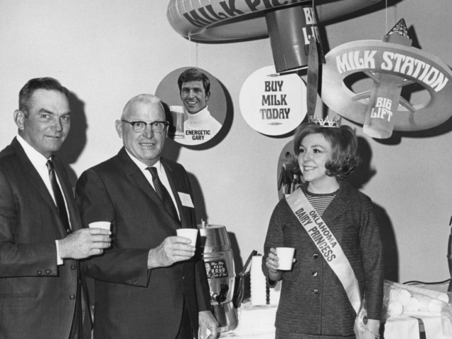 Emmett Carter of Purcell, Vice President of American Dairy Association, and Roy Counts of Dover, Secretary of Milk Producers Inc., take a milk break with Oklahoma Dairy Princess Quinetta Beagle of Arnett during a meeting in Oklahoma City in 1969.