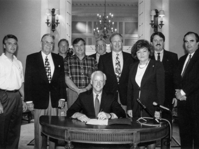 This photo was taken June 12, 1998, as Gov. Frank Keating’s signature on Oklahoma’s estate tax reform bill drew a large crowd of interested witnesses. Attending the ceremony in the Oklahoma State Capitol’s Blue Room were (left to right) OKFB General Counsel Richard Herren, OKFB President Jack Givens, OKFB Executive Director Matt Wilson, Mason Mungle, Rep. Larry Ferguson, Sen. Owen Laughlin, Rep. Mary Easley, Agriculture Commissioner Dennis Howard, and Director of State Finance Tom Daxon.
